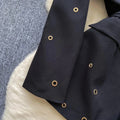 Close-up of black fabric with eyelet details on a white surface, part of a Two Piece Suit ensemble.