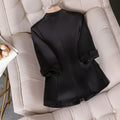 Elegant slim waist black jacket blazer for women with cropped sleeves on a beige tufted chair.